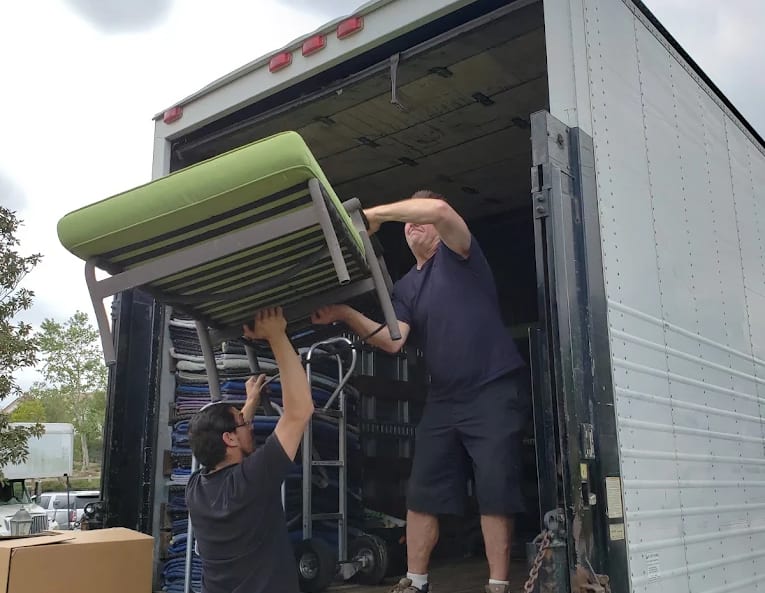 Two BEST MOVE movers lifting a sofa up into the back of the truck, moving blankets stacked behind them