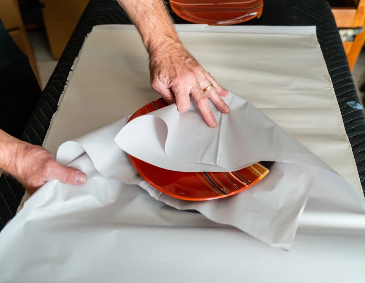 A BEST MOVE packer’s hands wrapping a glazed dinner plate in clean packing paper