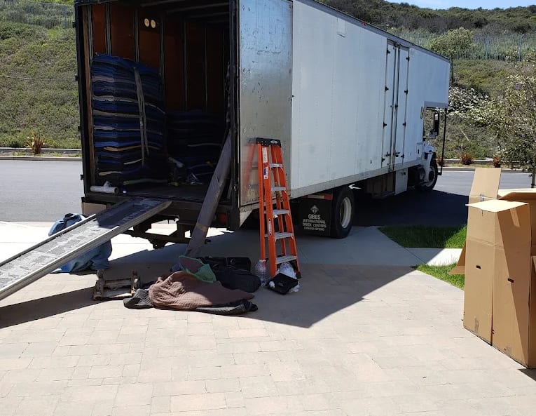 A BEST MOVE truck with its ramp down on a paved driveway, moving blankets stacked inside and cartons waiting to load